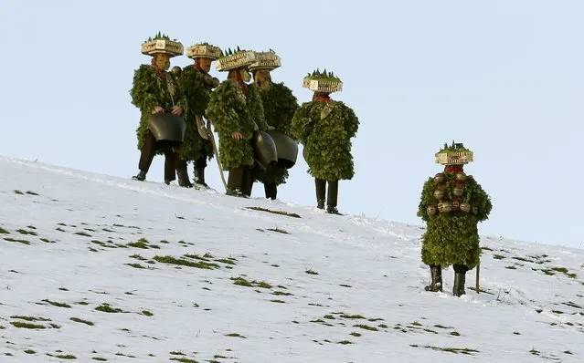 Men dressed as “Chlaeuse”, figures that scare away evil spirits, carry round bells and cowbells as they stand on a partially snow-covered meadow during the traditional "Syvesterchlausen" near the northeastern village of Urnaesch January 13, 2015. (Photo by Arnd Wiegmann/Reuters)