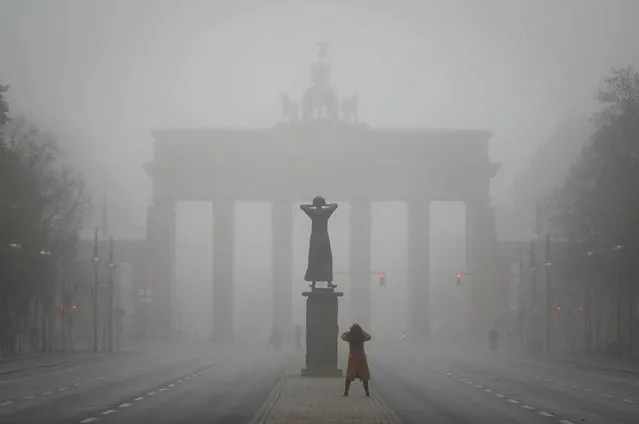 A woman photographs the Brandenburg Gate and the statue “The Crier” by Gerhard Marcks on a foggy morning in Berlin Wednesday, November 16, 2016. (Photo by Kay Nietfeld/DPA via AP Photo)
