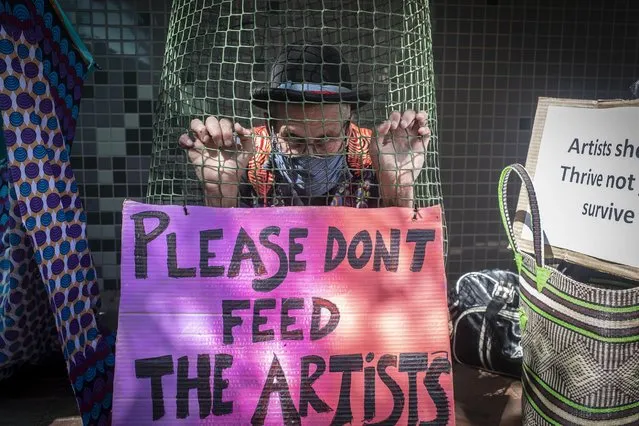 An artist sits behind a net and placard as artist, including clowns and puppeteers demonstrate during a week-long demonstration calling for answers from the National Arts Council about the COVID-19 coronavirus stimulus package, in Johannesburg, South Africa, 18 March 2021. The artist are demonstrating because the PESP (Presidential Stimulus Package) that was promised in 2020 to help struggling artists effected by a loss of work due to the pandemic has been blighted by corruption allegations. (Photo by Kim Ludbrook/EPA/EFE)
