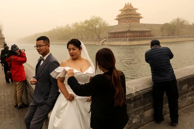 A couple poses during their wedding photoshoot while others take pictures of the scenery near the Forbidden City, as the city is hit by sandstorm, in Beijing, China on March 15, 2021. (Photo by Tingshu Wang/Reuters)