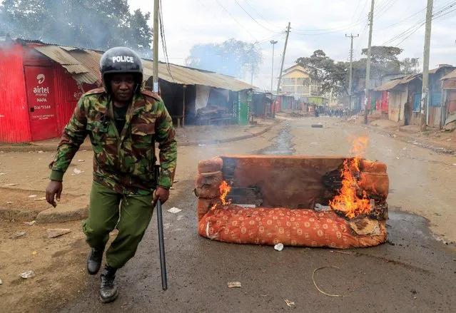 A riot police officer runs next to a burning sofa, as supporters of Kenya's opposition leader Raila Odinga of the Azimio La Umoja (Declaration of Unity) One Kenya Alliance participate in an anti-government protest against the imposition of tax hikes by the government in Nairobi, Kenya on July 19, 2023. (Photo by Thomas Mukoya/Reuters)
