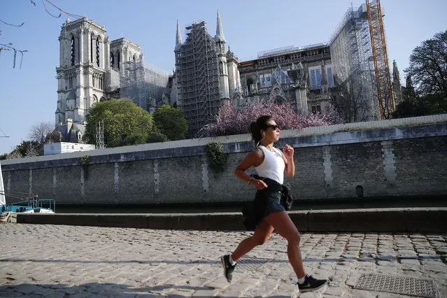 A woman jogs in front of Notre Dame cathedral, Thursday, April 15, 2021 in Paris. Two years after a fire tore through Paris' most famous cathedral and shocked the world, French President Emmanuel Macron is visiting the building site that Notre Dame has become to show that French heritage has not been forgotten despite the coronavirus. (Photo by Francois Mori/AP Photo)