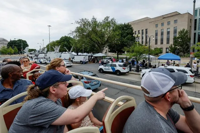 Tourists atop a double-decker tour bus pass by assembled reporters, law enforcement officers and demonstrators as they wait for former U.S. President Donald Trump, who is facing federal charges related to attempts to overturn his 2020 election defeat, to arrive at U.S. District Court in Washington, U.S., August 3, 2023. (Photo by Jonathan Ernst/Reuters)
