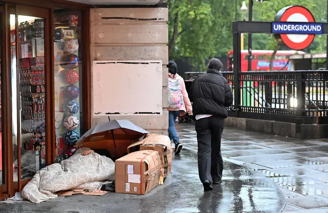 A pedestrian walks in the rain past a rough sleeper in their makeshift bed and camp outside a closed shop on Oxford Street, at daybreak in London on August 2, 2023. A report released by the Combined Homelessness and Information Network (Chain) on July 31, 2023, found that the number of new people sleeping rough in London in spring and early summer had risen by 12% on the same period last year. The report found that 3,272 people were recorded as sleeping rough in the capital, up 9% on the total figure for April-June 2022. (Photo by Justin Tallis/AFP Photo)