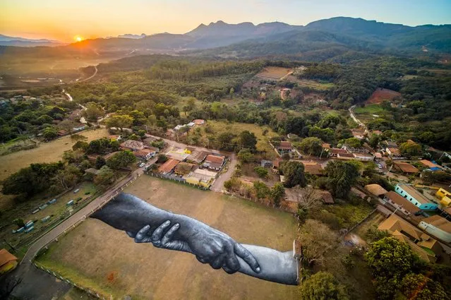 Handout picture release by Saype shows an aerial view of French artist Saype's work of art, in gigantic dimensions, that pays tribute to the victims and those affected by the collapse of the Corrego do Feijao dam of mining company Vale at Corrego do Feijao football field in Brumadinho, state of Minas Gerais, Brazil on July 24, 2022. Brumadinho is one of the 30 cities taking part in the Saype's worldwide project Beyond Walls. (Photo by Handout/SAYPE/AFP Photo)