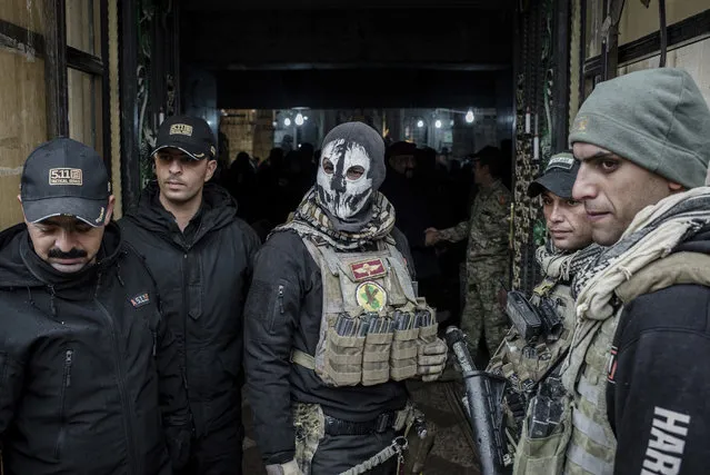 Iraqi forces guard the entrance to a Christmas Eve's Mass at the Assyrian Orthodox church of Mart Shmoni, in Bartella, Iraq, Saturday, December 24, 2016. For the 300 Christians who braved rain and wind to attend the mass in their hometown, the ceremony provided them with as much holiday cheer as grim reminders of the war still raging on around their northern Iraqi town and the distant prospect of moving back home. Displaced when the Islamic State seized their town in 2014, they were bused into the town from Irbil, capital of the self-ruled Kurdish region, where they have lived for more than two years. (Photo by Cengiz Yar/AP Photo)
