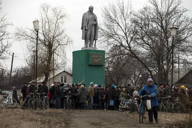 People queue for free food distributed by pro-Russian rebels next to a monument of the Soviet state founder Vladimir Lenin in the village of Chornukhyne near the town of Debaltseve, north-east from Donetsk, March 12, 2015. (Photo by Marko Djurica/Reuters)