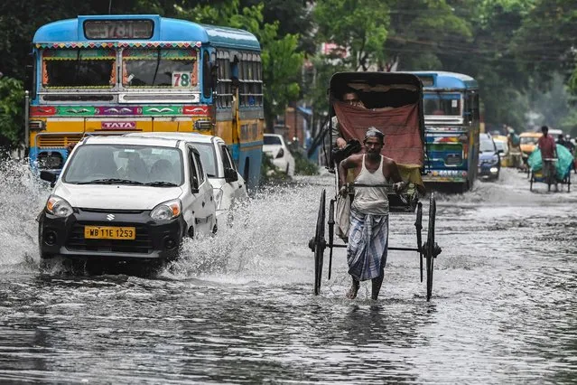 A hand-rickshaw puller ferrying a passenger wades through a waterlogged street after it rained in Kolkata on July 29, 2021. (Photo by Dibyangshu Sarkar/AFP Photo)