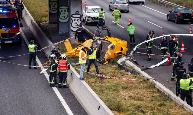 Emergency workers stand next to a helicopter that crashed on a Madrid motorway ring road, hitting a car and injuring people, in Madrid, Spain on December 1, 2023. (Photo by Juan Medina/Reuters)