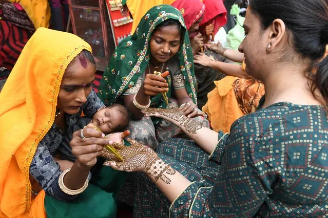 Women get their hands decorated with henna on the eve of the Karva Chauth festival, in which married women fast one whole day and offer prayers to the moon for the welfare, prosperity, and longevity of their husbands, in Amritsar on October 23, 2021. (Photo by Narinder Nanu/AFP Photo)