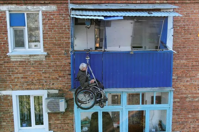 Local resident Alexander Yudin ascends to the balcony of his apartment on the third floor using a self-constructed elevator in the town of Timashevsk in the Krasnodar region, Russia, November 17, 2021. Electrician Alexander Yudin, who lost his leg in a car accident several decades ago and then lamed his second leg three years ago, constructed a solar-powered balcony elevator to leave his three-storey block of flats lacking any facilities for low-mobility residents. Picture taken with a drone. (Photo by Sergey Pivovarov/Reuters)