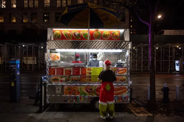 A person dressed in a Santa Claus costume orders from a food cart during Santacon as it continues into the night in the East Village on December 11, 2021 in New York City. Santacon returned this year after it was cancelled in 2020 due to the coronavirus pandemic. Santacon is an annual Christmas themed pub crawl raising money for charity. People officially participating in Santacon this year were required to be vaccinated in order to enter the bars affiliated with it. (Photo by Alexi Rosenfeld/Getty Images)