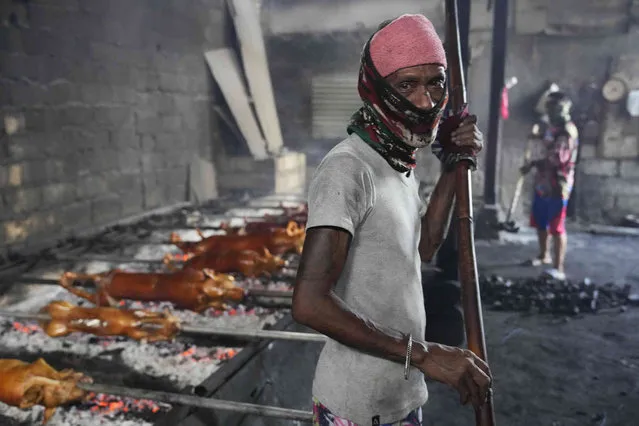 A worker wearing a mask to prevent the spread of the coronavirus cooks roasted pigs in Manila, Philippines on Christmas Eve, Friday, December 24, 2021. (Photo by Aaron Favila/AP Photo)