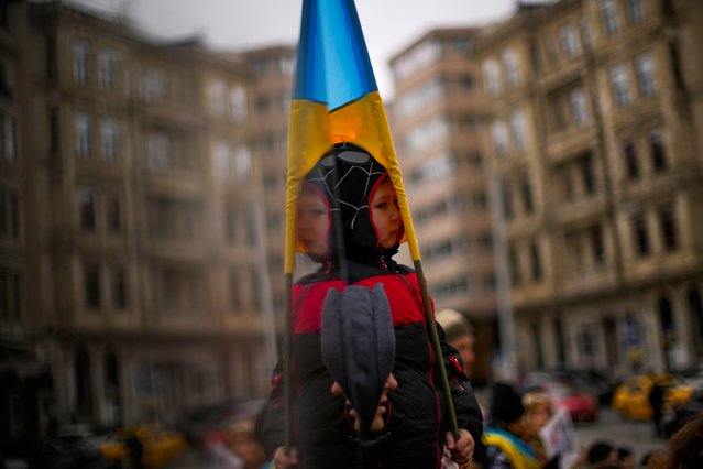 A child, partially reflected in a glass, holds a Ukraine flag during a protest by pro-Ukraine people against Russia's invasion of Ukraine, in Istanbul, Turkey, Monday, March 7, 2022. Russia announced yet another cease-fire and a handful of humanitarian corridors to allow civilians to flee Ukraine. Previous such measures have fallen apart and Moscow's armed forces continued to pummel some Ukrainian cities with rockets Monday. (Photo by Francisco Seco/AP Photo)
