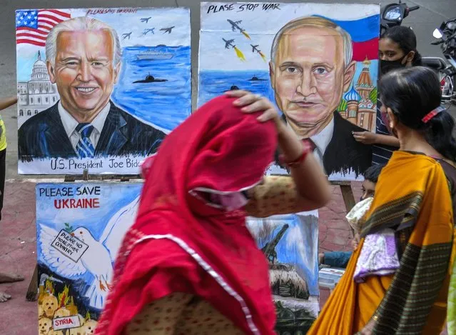 A woman adjusts her sari as she walks past as students of an art school display their art works calling for peace amid fears of a Russian offensive on Ukraine on a pavement in Mumbai, India, Monday, February 21, 2022. (Photo by Rafiq Maqbool/AP Photo)