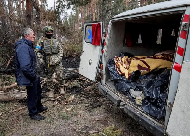 Ukrainian service members and residents stand near the bodies of civilians, which according to residents were killed by Russian soldiers, in the village of Motyzhyn, in the Kyiv region, Ukraine on April 4, 2022. (Photo by Gleb Garanich/Reuters)