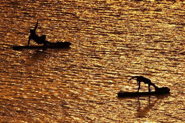 People do yoga poses on paddleboards at sunset as the heat index tops 100 degrees at Olathe Lake, Monday, July 15, 2024, in Olathe, Kan. (Photo by Charlie Riedel/AP Photo)