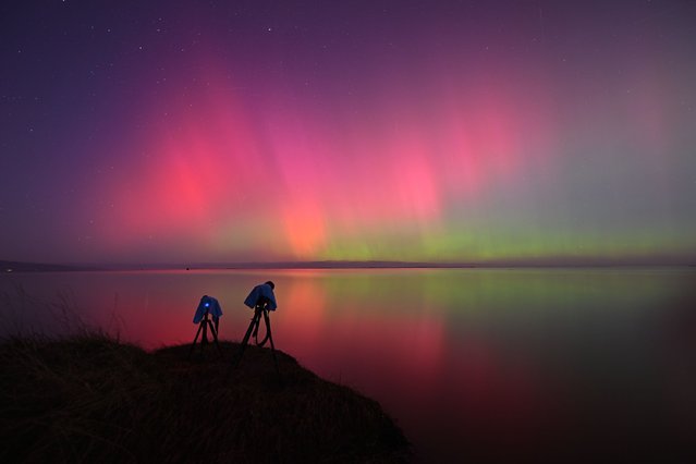 A photographer's camera setup is seen as the Aurora Australis, also known as the Southern Lights, glow on the horizon over waters of Lake Ellesmere on the outskirts of Christchurch on May 11, 2024. The most powerful solar storm in more than two decades struck Earth, triggering spectacular celestial light shows from Tasmania to Britain – and threatening possible disruptions to satellites and power grids as it persists into the weekend. (Photo by Sanka Vidanagama/AFP Photo)