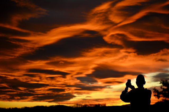 A person takes pictures with a smartphone of the sky illuminated during sunset behind the Jura mountains in Gros-de-Vaud Region on Christmas eve, in Daillens, southwestern Switzerland on December 24, 2023. (Photo by Laurent Gilliéron/EPA/EFE)