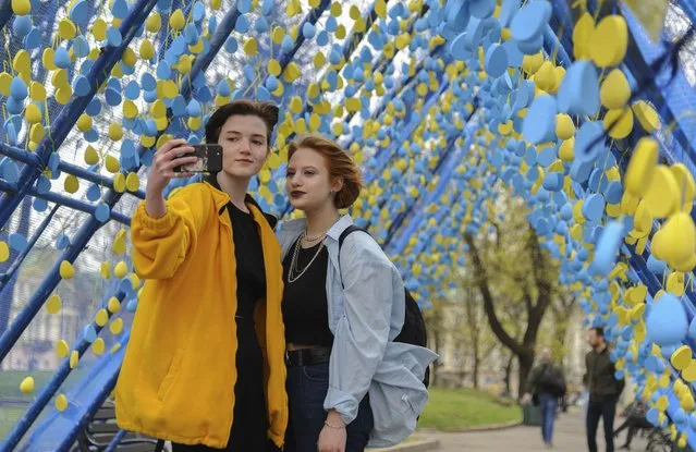 Ukrainians pose for a selfie picture at an installation called “A life corridor” in the downtown of Western Ukrainian city of Lviv, Ukraine, 15 April 2022, to pay respect to Ukrainians who died during the Russian invasion. The painted eggs are the symbol of life, incoming Easter, and memory for people who couldn't to went the Green corridors for evacuation because they so often were shelled by Russian troops. The form of installation was made like home roofs as millions of Ukrainians were obliged to leave their homes to save themselves from the war. Russian troops entered Ukraine on 24 February resulting in fighting and destruction in the country and triggering a series of severe economic sanctions on Russia by Western countries. (Photo by Mykola Tys/EPA/EFE)