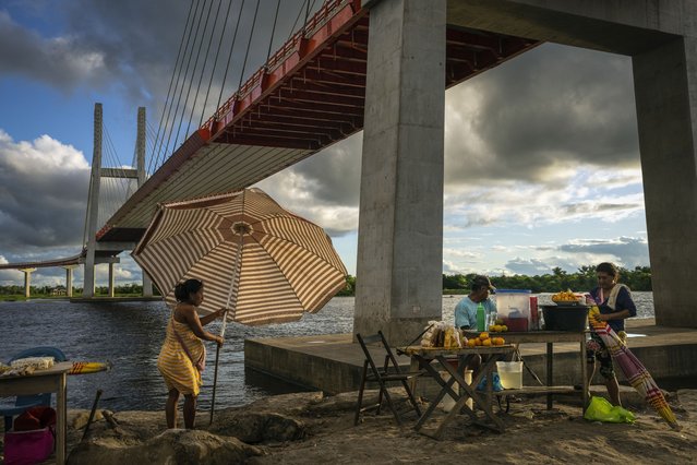 Vendors set up food stands under a bridge that is part of a federal highway project that extends over the Nanay River, in Iquitos, Peru, Monday, May 27, 2024. The project, which spans 188 kilometers (117 miles), is intended to connect Iquitos, the main city in Peru's Amazon, with the El Estrecho district on the Colombian border. (Photo by Rodrigo Abd/AP Photo)