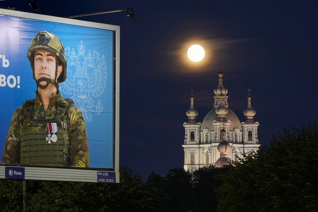 The supermoon is seen over the Smolny Cathedral in St. Petersburg, Russia, Tuesday, August 20, 2024, with an advertising billboard displaying a Russian soldier, participants of the military operation in Ukraine, in the foreground. (Photo by Dmitri Lovetsky/AP Photo)