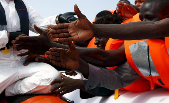 Migrants reach out to grab hold of Migrant Offshore Aid Station (MOAS) rescuers on a RHIB (Rigid-hulled inflatable boat) before being taken to the MOAS ship MV Phoenix some 20 miles (32 kilometres) off the coast of Libya, August 3, 2015. (Photo by Darrin Zammit Lupi/Reuters)
