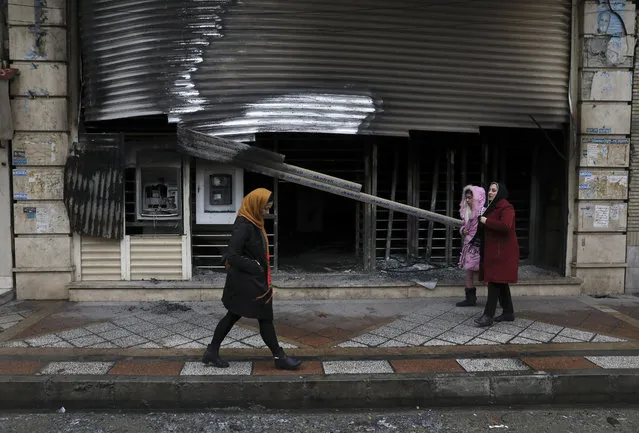 People walk past a bank that was burned during recent protests, in Shahriar, Iran, some 40 kilometers (25 miles) southwest of the capital, Tehran, Wednesday, November 20, 2019. Protests over government-set gasoline prices rising struck at least 100 cities and towns, spiraling into violence that saw banks, stores and police stations attacked and burned. (Photo by Vahid Salemi/AP Photo)