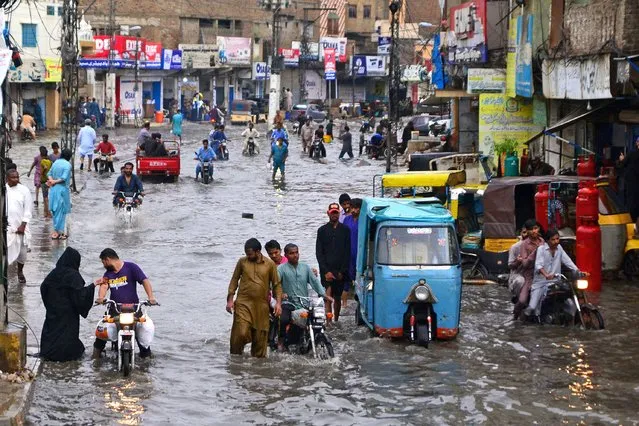 Commuters make their way through a flooded street during monsoon rainfall in Hyderabad, Pakistan on July 24, 2022. (Photo by Akram Shahid/AFP Photo)