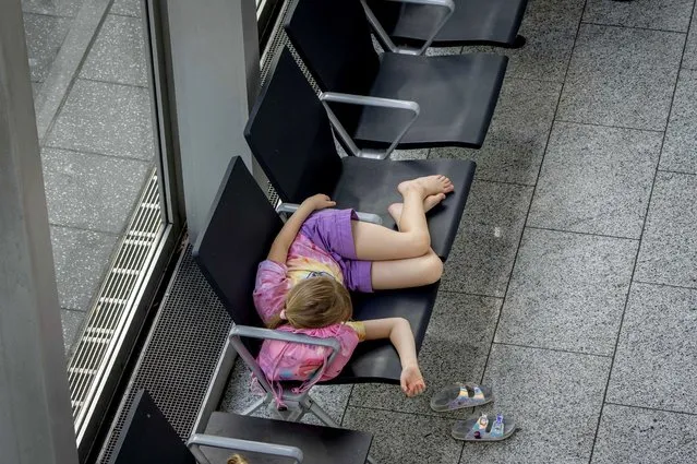 A girl sleeps on chairs at the international airport in Frankfurt, Germany, Wednesday, July 27, 2022. Lufthansa went for a 24-hours-strike on Wednesday, most of the Lufthansa flights had to be cancelled. (Photo by Michael Probst/AP Photo)