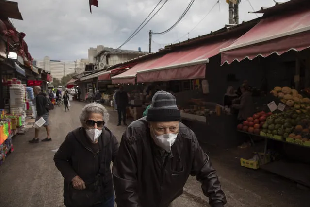 An elderly couple wear face masks as they shop at a food market in Tel Aviv, Israel, Tuesday, March 17, 2020. The head of Israel's shadowy Shin Bet internal security service said Tuesday that his agency received Cabinet approval overnight to start deploying its counter-terrorism tech measures to help curb the spread of the new coronavirus in Israel. For most people, the virus causes only mild or moderate symptoms. For some it can cause more severe illness. (Photo by Oded Balilty/AP Photo)