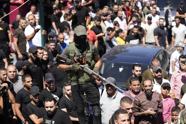 A gunman stands guard as Palestinian mourners gather for the funerals of Muhammad Al-Azizi and Aboud Sobh, two Palestinian militants killed when Israeli troops and special forces on an arrest mission exchanged fire with Palestinians barricaded in a house in the West Bank city of Nablus, Sunday, July 24, 2022. Israeli troops shot and killed two Palestinians Sunday, the Palestinian rescue service said, as the Israeli military said it confronted armed men during overnight operations in the West Bank. (Photo by Majdi Mohammed/AP Photo)