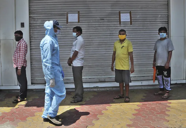People wearing masks stand in a queue to receive food being distributed during lockdown in Mumbai, India, Sunday, March 29, 2020. Indian Prime Minister Narendra Modi apologized to the public on Sunday for imposing a three-week national lockdown, calling it harsh but “needed to win” the battle against the coronavirus pandemic. (Photo by Rafiq Maqbool/AP Photo)