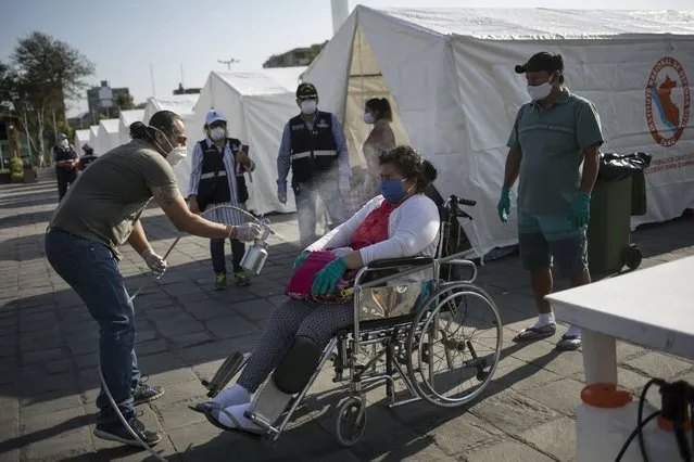 A woman is sprayed with disinfectant at a makeshift camp in Lima previous to her return to her home province in Piura, Peru, Thursday, April 23, 2020. After not being allowed to leave the capital because the strict quarantine rules amid the new coronavirus pandemic, day laborers and informal workers are now allowed to travel home but local authorities are screening them for the disease before letting them travel. (Photo by Rodrigo Abd/AP Photo)