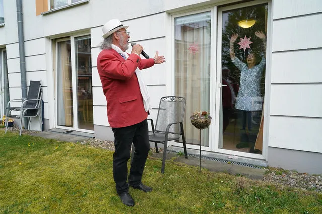 Resident Johanna Pfeiffer, 96, looks on from her room as singer Alf Weiss performs live at the Hermann Radtke Haus nursing home during the novel coronavirus crisis on April 29, 2020 in Berlin, Germany. The home, which has a total of 195 residents, has seen its share of Covid-19 infections, from which eight residents have died. Of the 12 remaining infected residents eight are recovering, according to the home's manager. Local performer Alf Weiss sang a mix of schmalzy hits for two hours outside in the courtyard of the home. Some residents emerged with walkers or electric wheelchairs to watch and listen, while others looked on from the windows of their rooms as a few nursing staff members danced. Many senior care facilities across Germany have been hit with Covid-19 infections. The Hermann Radtke Haus is part of the Diakonie Simeon gGmbH, a caregiving and social work organization of the Protestant Church. (Photo by Sean Gallup/Getty Images)