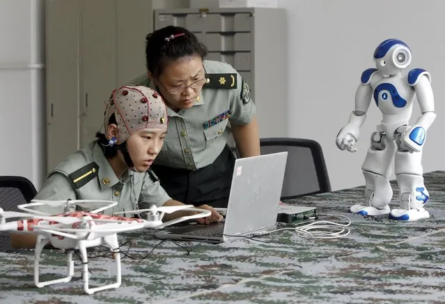 A student (L) and an instructor look at a computer as they demonstrate using a headset to control robots with her mind, at the People's Liberation Army (PLA) Information Engineering University, in Zhengzhou, Henan province, China, August 7, 2015. The robots can be controlled through the headset to go different directions, turn their heads and pick up objects, local media reported. (Photo by Reuters/Stringer)