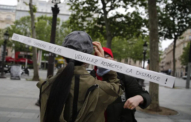 A woman has a banner attached to her cap the reads “This is a 1-meter long hat, please respect the distance” Monday, May 11, 2020 in Paris. The French began leaving their homes and apartments for the first time in two months without permission slips as the country cautiously lifted its lockdown. Clothing stores, coiffures and other businesses large and small were reopening on Monday – with strict precautions to keep the coronavirus at bay. (Photo by Francois Mori/AP Photo)