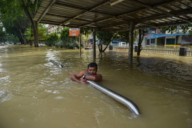 A man holds onto barriers as he waits to be evacauted by a rescue team in Shah Alam, Selangor on December 20, 2021, as Malaysia faces some of its worst floods for years. (Photo by Arif Kartono/AFP Photo)