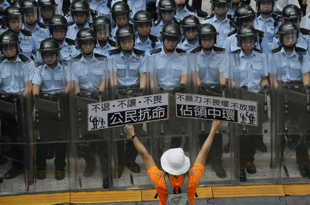 A protester raises placards that read “Occupy Central”, right, and “Civil disobedience” in front of riot policemen outside the government headquarters in Hong Kong, Saturday, September 27, 2014. Riot police on Saturday arrested scores of students who stormed the government headquarters compound in Hong Kong's Central district during a night of scuffles to protest China's refusal to allow genuine democratic reforms in the semiautonomous region. (Photo by Vincent Yu/AP Photo)