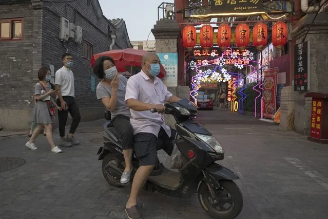 Residents wearing masks to curb the spread of the coronavirus past by lanterns and neon lights promoting a restaurant in Beijing on Friday, June 26, 2020. Even as Beijing appears to have contained the latest outbreak, businesses are still reeling from the prolonged impact of the coronavirus on the economy. (Photo by Ng Han Guan/AP Photo)