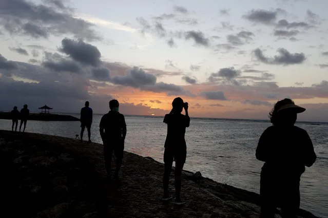People watch the sunrise at a beach in Bali, Indonesia on Thursday, July 9, 2020. Indonesia's resort island of Bali reopened after a three-month virus lockdown Thursday, allowing local people and stranded foreign tourists to resume public activities before foreign arrivals resume in September. (Photo by Firdia Lisnawati/AP Photo)