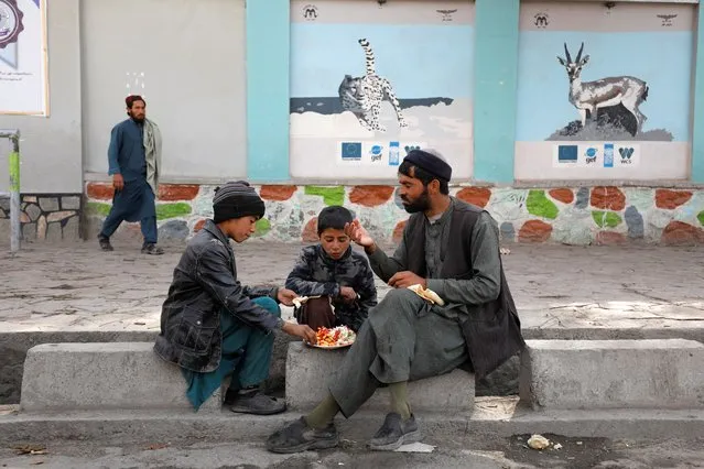 Afgan man and his children eat food in a street in Kabul, Afghanistan on November 9, 2022. (Photo by Ali Khara/Reuters)