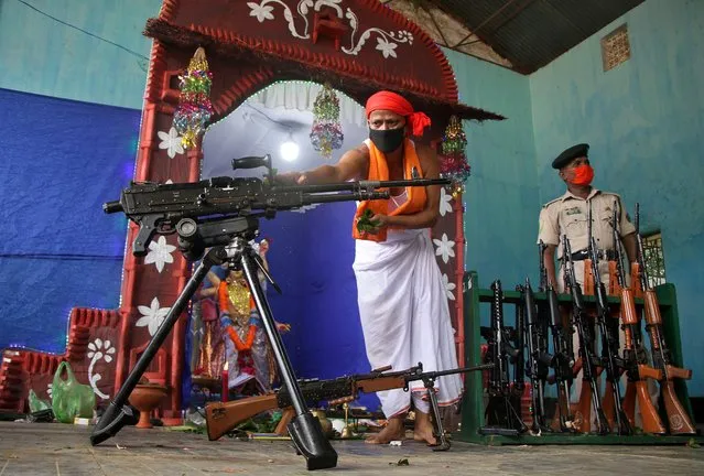 A Hindu priest wearing a protective mask worships next to weapons belonging to Tripura State Rifles during the Vishwakarma Puja, the festival of the Hindu deity of architecture and machinery, amid the spread of the coronavirus disease (COVID-19), in Agartala, India, September 17, 2020. (Photo by Jayanta Dey/Reuters)