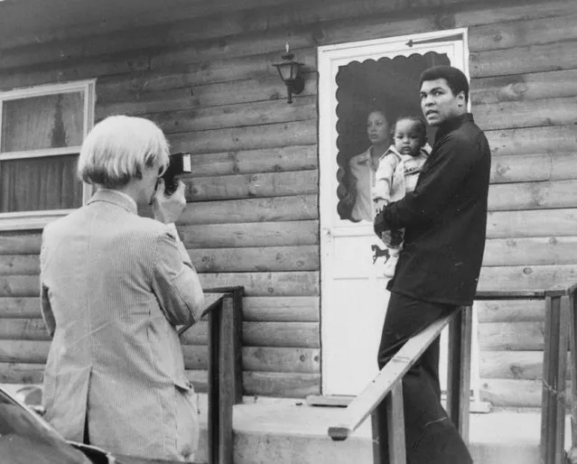 Pop artist Andy Warhol, left, is shown photographing Muhammad Ali, his infant daughter, Hanna, and wife, Veronica, Thursday, August 18, 1977, at Ali's training camp in Deer Lake, Pa. (Photo by AP Photo)