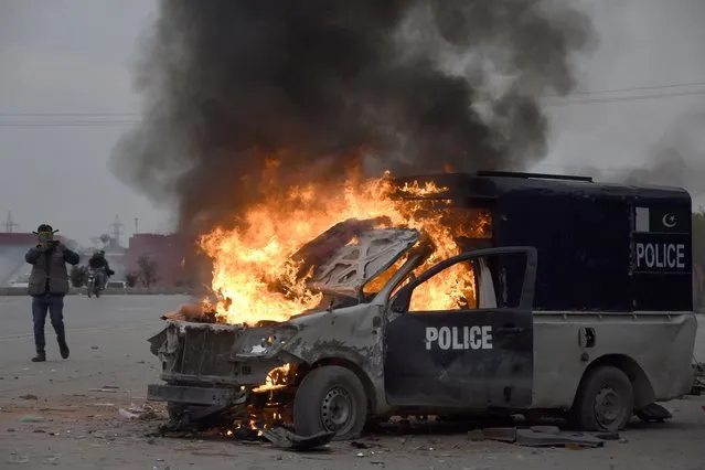 A man films with his mobile phone to a burning police vehicle following the clashes between police and the supporters of former Prime Minister Imran Khan, at outside the a court, in Islamabad, Pakistan, March 18, 2023. (Photo by W.K. Yousafzai/AP Photo)