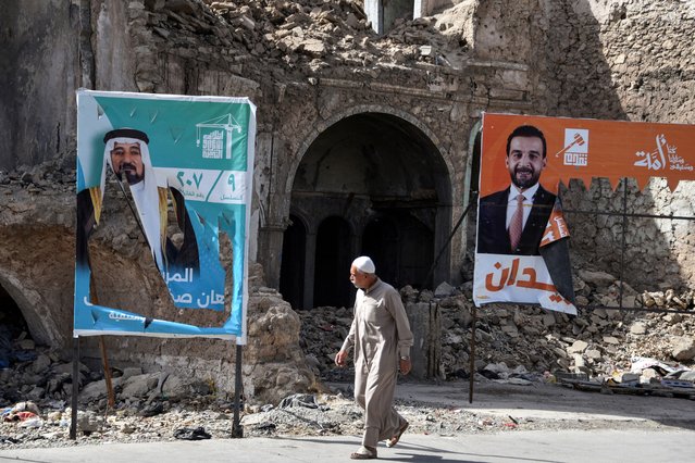 A man walks past banners placed infront of war damaged building depicting political candidates from rival blocs, competing for a seat in the Iraqi Council of Representatives, days before the Parliamentary elections, in Old Mosul, northern Iraq, on October 28, 2025. Parliamentary elections are scheduled to be held in Iraq on 11 November 2025, which will determine the 329 members of Iraq's Council of Representatives, who are responsible for electing the country's president and approving the appointment of the prime minister. (Photo by Zaid Al-Obeidi/AFP Photo)