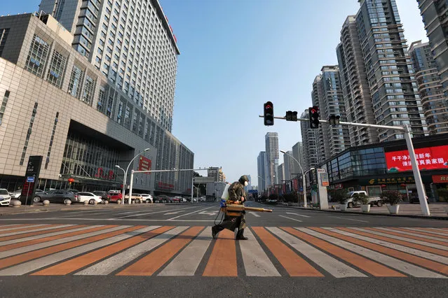 A worker with sanitizing equipment crosses the road in front of a hospital in Yichang city of Hubei, the province hit hardest by the novel coronavirus outbreak, China on February 12, 2020. (Photo by Reuters/China Daily)