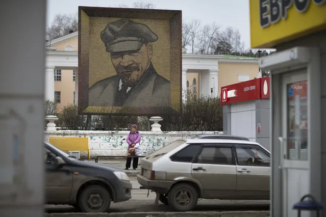 In this Thursday, October 27, 2016 photo, a woman waits for a bus at a bus stop in front of a huge portrait of the Soviet Union leader Vladimir Lenin in the central square of a small town just outside Yekaterinburg, Russia. (Photo by Alexander Zemlianichenko/AP Photo)