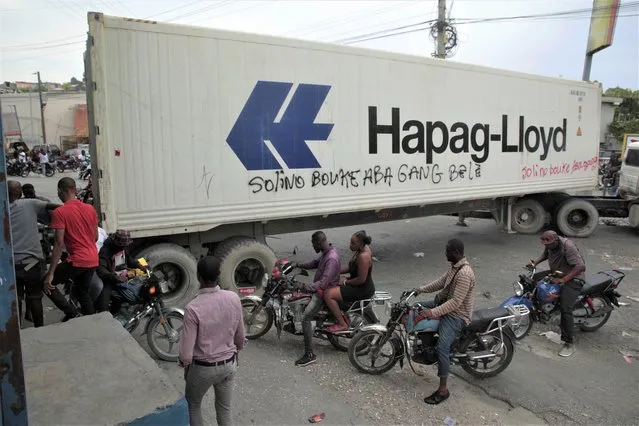 Taxi drivers walk past a truck blocking a street as part of an anti-gang protest in Port-au-Prince, Haiti, Tuesday, April 25, 2023, a day after a mob in the Haitian capital pulled 13 suspected gang members from police custody at a traffic stop and beat and burned them to death with gasoline-soaked tires. (Photo by Joseph Odelyn/AP Photo)