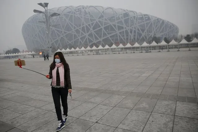 A woman wearing a mask protecting from extreme smog takes picture in front of the National Stadium, or the Bird's Nest in Beijing December 8, 2015 as China's capital issues its first ever "red alert" for pollution. (Photo by Damir Sagolj/Reuters)